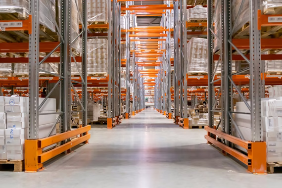 A long aisle between tall pallet racking stacked on both sides with shrink-wrapped pallets