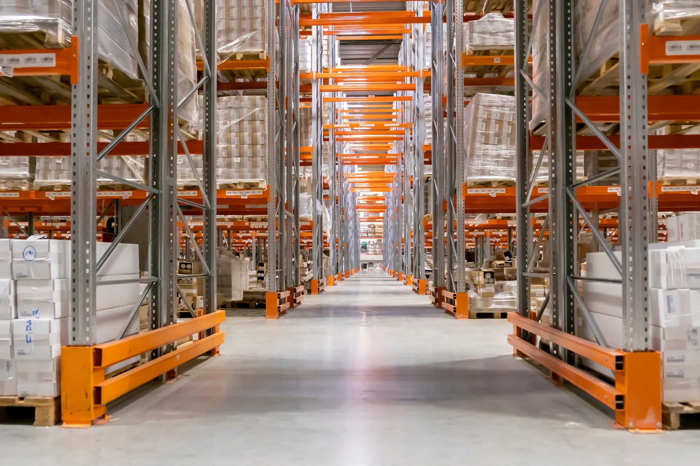 A long aisle between tall pallet racking stacked on both sides with shrink-wrapped pallets
