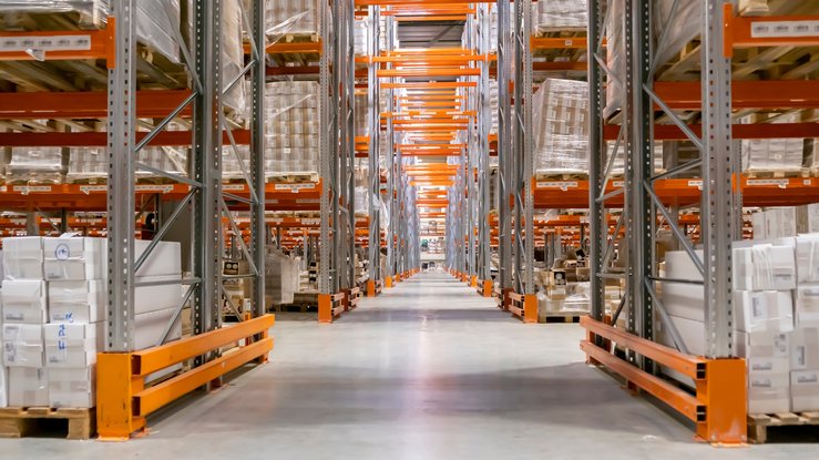 A long aisle between tall pallet racking stacked on both sides with shrink-wrapped pallets — distributor and wholesaler insurance in Vermont