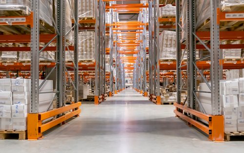 A long aisle between tall pallet racking stacked on both sides with shrink-wrapped pallets — warehouse and distributor insurance in Oklahoma