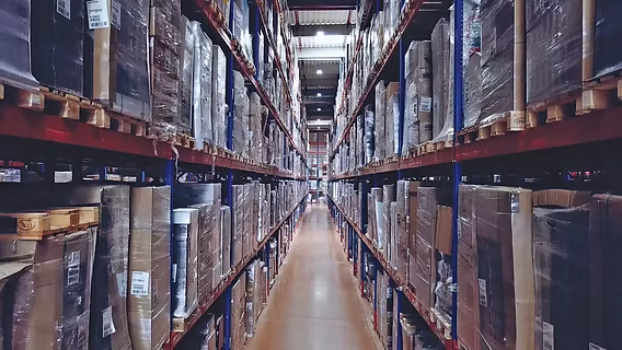 A narrow aisle running between tall racks of shrink-wrapped pallets in a warehouse — warehouse and distributor insurance in Idaho