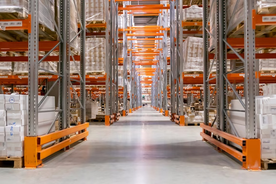 A long aisle between tall pallet racking stacked on both sides with shrink-wrapped pallets