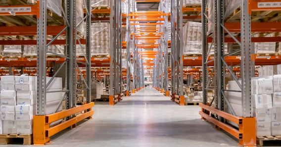 A long aisle between tall pallet racking stacked on both sides with shrink-wrapped pallets — warehouse insurance in Kansas
