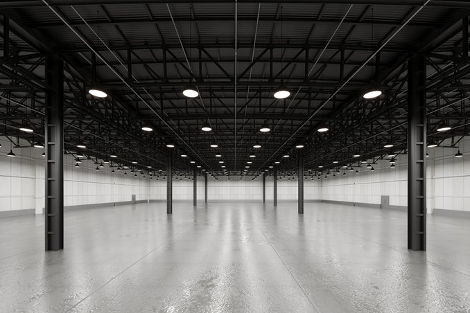 An empty warehouse interior with exposed steel roof framing and rows of pendant high-bay lights above a bare floor — warehouse insurance in North Carolina