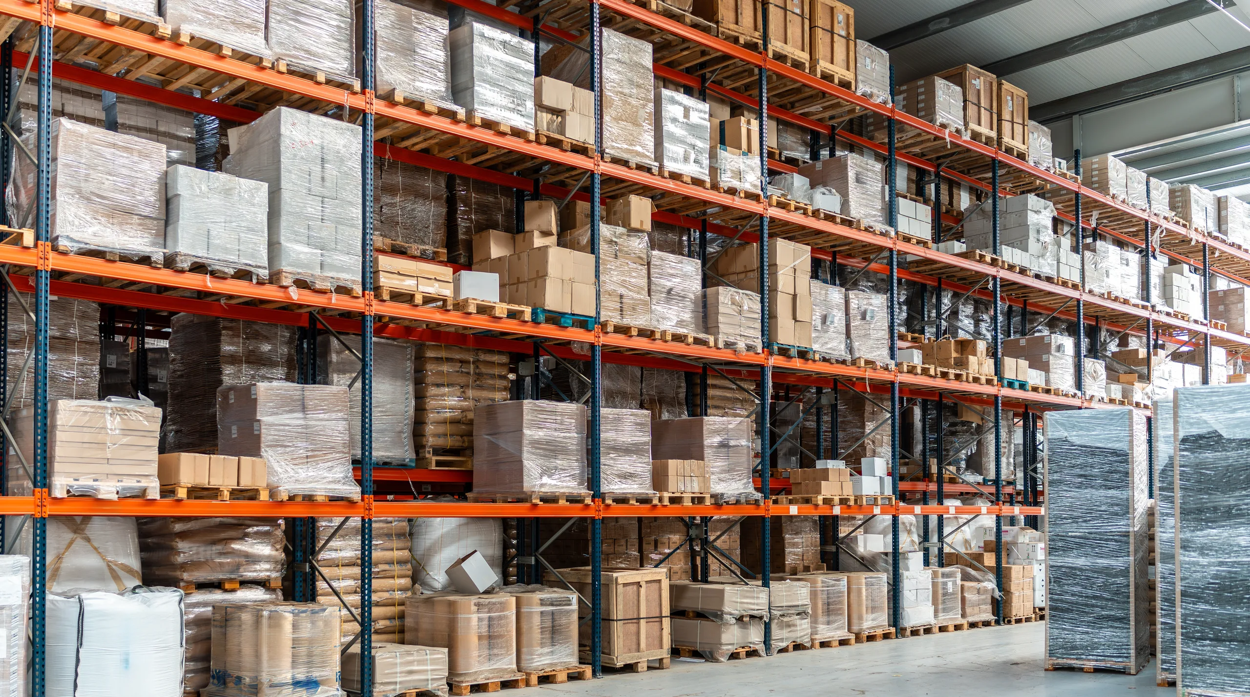A run of pallet racking filled with wrapped pallets and cartons on several levels above floor-level stock — warehouse insurance in Oklahoma