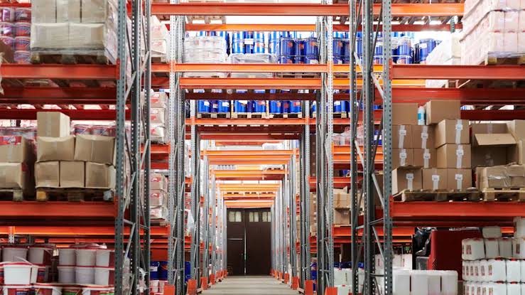 Orange pallet racking stacked with pails, drums and cartons receding down a warehouse aisle — warehouse insurance in Idaho